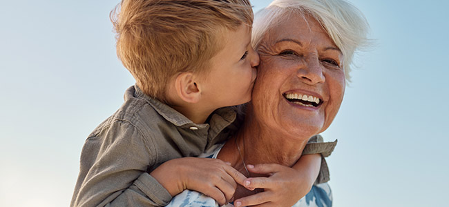 kiss, child and grandmother in a park with love, care and freedom for happiness in retirement. senior, smile and portrait of a woman with hug from a kid and kissing in nature or park with piggyback