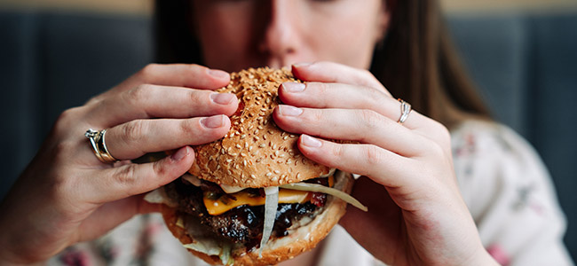 Hamburger From Hell Takes a Bite out of Restaurant’s Profits & Reputation fast food burger eat. pretty young happy woman eating tasty hamburger. junk food concept.